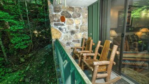 Pared exterior de piedra con un banco y sillas de madera, una puerta de cristal y una barandilla verde.