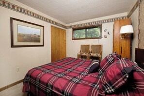 A bedroom with a plaid bedspread, a framed picture on the wall, a window, and a lamp.