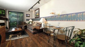 Una sala de estar acogedora con un sofá, una mesa de comedor con sillas, una chimenea y un ventanal con vistas a árboles.