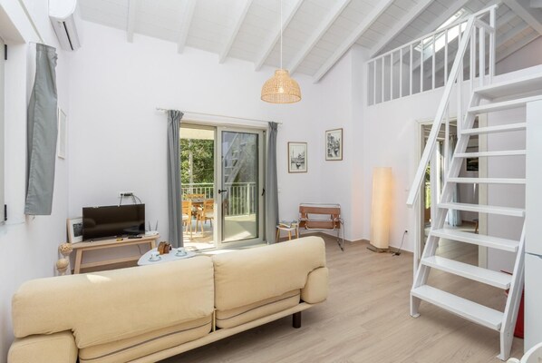 A spacious living room with a sofa, a TV, a table with a lamp, and a staircase.