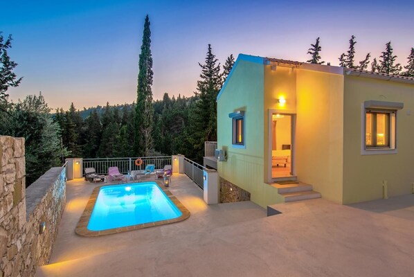 A modern villa with a swimming pool, outdoor seating, and a stone wall.