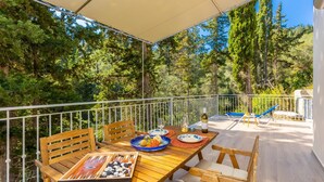 Une terrasse en bois avec une table dressée pour le repas, entourée d’une balustrade blanche, donnant sur une zone boisée.