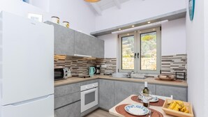 Une cuisine compacte avec des meubles gris, un four à micro-ondes, une bouilloire et une fenêtre donnant sur un espace verdoyant.