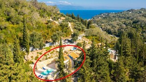 Une propriété située sur une colline, dotée d’une piscine, entourée d’une végétation luxuriante et offrant une vue sur la mer.