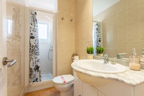 Un baño con ducha, inodoro, lavamanos y espejo.