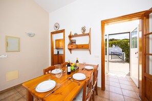 Ein Essbereich mit einem Holztisch, gedeckt für vier Personen, einer Uhr an der Wand und Blick ins Freie durch eine Glastür.