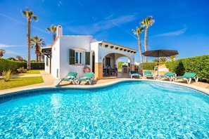A pool with lounge chairs, a patio area, and palm trees.
