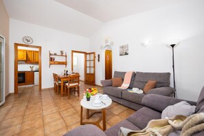 Een woonkamer met een bank, een eettafel met stoelen en een keuken met houten kastjes.
