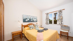 Un dormitorio con una cama, una mesita de noche, un armario de madera, una ventana con cortinas y un cuadro en la pared.