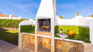 Cocina exterior con diseño de piedra y azulejos, una parrilla y un frutero con plátanos y naranjas.