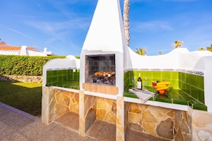 An outdoor kitchen with a stone and tile design, a grill, and a fruit bowl with bananas and oranges. - Villa Juana Large Private Pool, A/C, WiFi (Cap d'Artrutx)