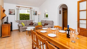 Un comedor con una mesa de madera dispuesta para cuatro personas, un sofá, un televisor y un armario.
