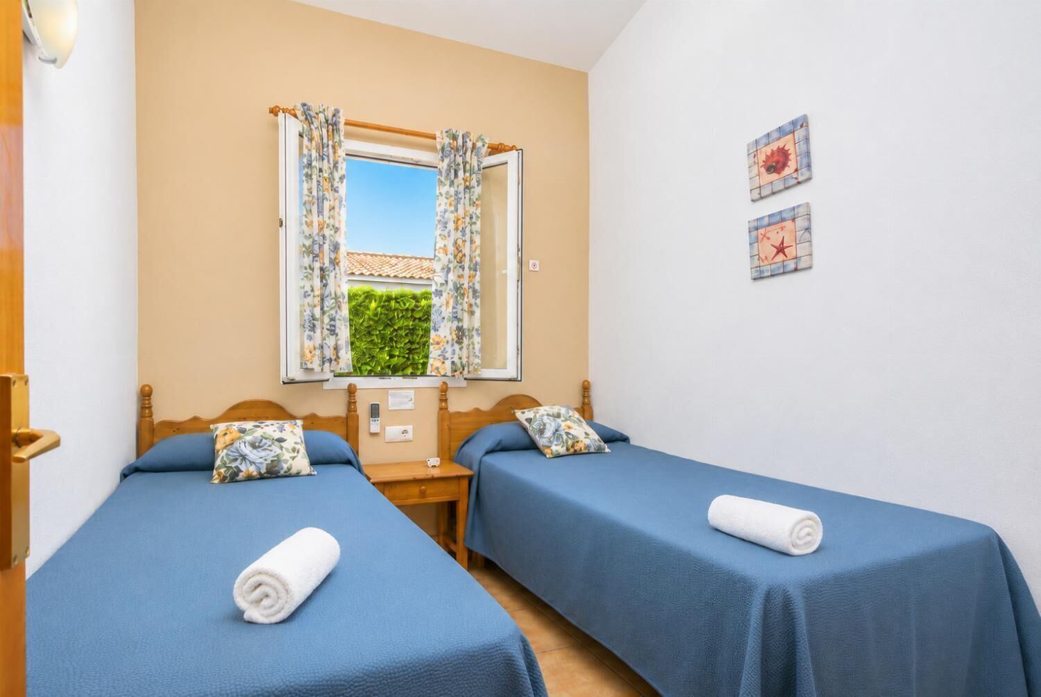 Une chambre avec deux lits, une fenêtre avec des rideaux, une horloge murale et une petite table.