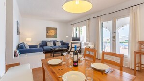 A dining area with a wooden table set for four, a blue sofa, and a painting on the wall. - Villa Binibety - Three Bedroom Villa, Sleeps 6 (Binibeca)