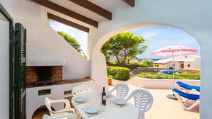An outdoor patio with a brick oven, white plastic chairs, and a table set for dining. - Villa Binibety - Three Bedroom Villa, Sleeps 6 (Binibeca)