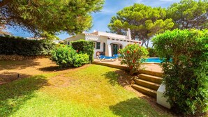 Une villa avec piscine, entourée d’une végétation luxuriante et d’une pelouse bien entretenue.