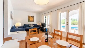 Un salon avec un canapé, une table à manger dressée avec des assiettes et des verres, un téléviseur et un tableau accroché au mur.
