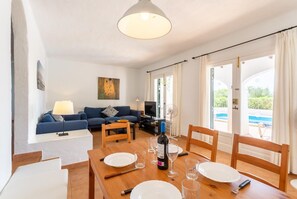 Ein Wohnzimmer mit einer Couch, einem Esstisch gedeckt mit Tellern und Gläsern, einem Fernseher und einem Bild an der Wand.