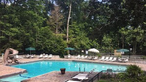 A swimming pool with lounge chairs and umbrellas, surrounded by trees. - Relax and Soak with a Mountain View! - Bear Watch 1011 (Gatlinburg)