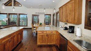 A modern kitchen with wooden cabinets, granite countertops, and a central island. There are pendant lights, a coffee maker, and a dishwasher. - Relax and Soak with a Mountain View! - Bear Watch 1011 (Gatlinburg)