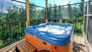A hot tub on a wooden deck with a view of a forest. - Relax and Soak with a Mountain View! - Bear Watch 1011 (Gatlinburg)