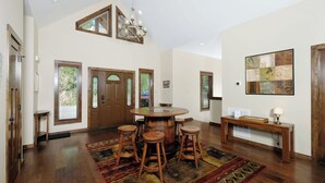 A spacious room with a wooden dining table, four stools, a chandelier, and a large window with blinds. - Relax and Soak with a Mountain View! - Bear Watch 1011 (Gatlinburg)