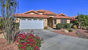 A residential house with a red-tiled roof, a white garage door, and a well-maintained garden with red flowers and cacti. - Casa Milan 3BR/5Beds-LaQuinta Hm Lic.065016 (La Quinta)
