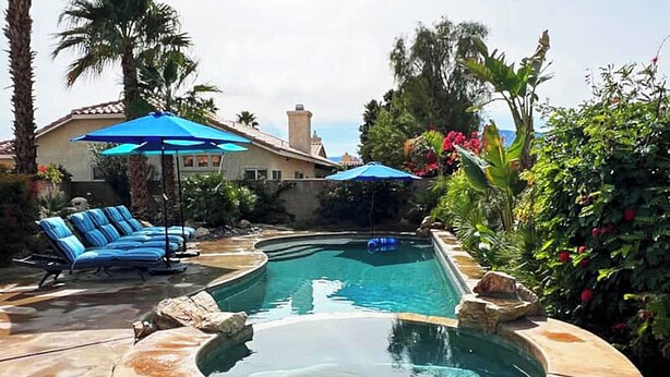 A hot tub surrounded by lounge chairs and umbrellas, with a pool and tropical plants in the background. - Casa Milan 3BR/5Beds-LaQuinta Hm Lic.065016 (La Quinta)