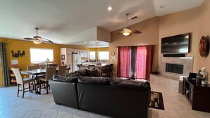 A spacious living area with a large black sofa, a dining table with chairs, a kitchen in the background, and a TV mounted on the wall. - Casa Milan 3BR/5Beds-LaQuinta Hm Lic.065016 (La Quinta)