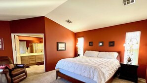 A bedroom with a large bed, a chair, a dresser, and a bathroom visible through an open door. - Casa Milan 3BR/5Beds-LaQuinta Hm Lic.065016 (La Quinta)