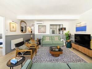 A modern living room with a green sofa, wooden chairs, a coffee table, and a TV.