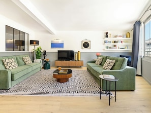 A modern living room with two green sofas, a coffee table, a TV, and a bookshelf with decorative items. - LivinParis | Luxury AC 3 Bedrooms Le Marais III (Paris)