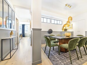 A modern dining area with a glass-top table, green upholstered chairs, and a patterned rug. - LivinParis | Luxury AC 3 Bedrooms Le Marais III (Paris)