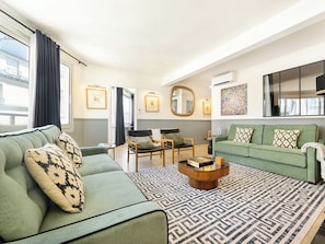 A modern living room with a green sofa, matching armchairs, a coffee table, and a patterned rug.