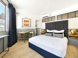 A hotel room with a large bed, a desk, a chair, and a window with curtains. - LivinParis | Luxury AC 3 Bedrooms Le Marais III (Paris)