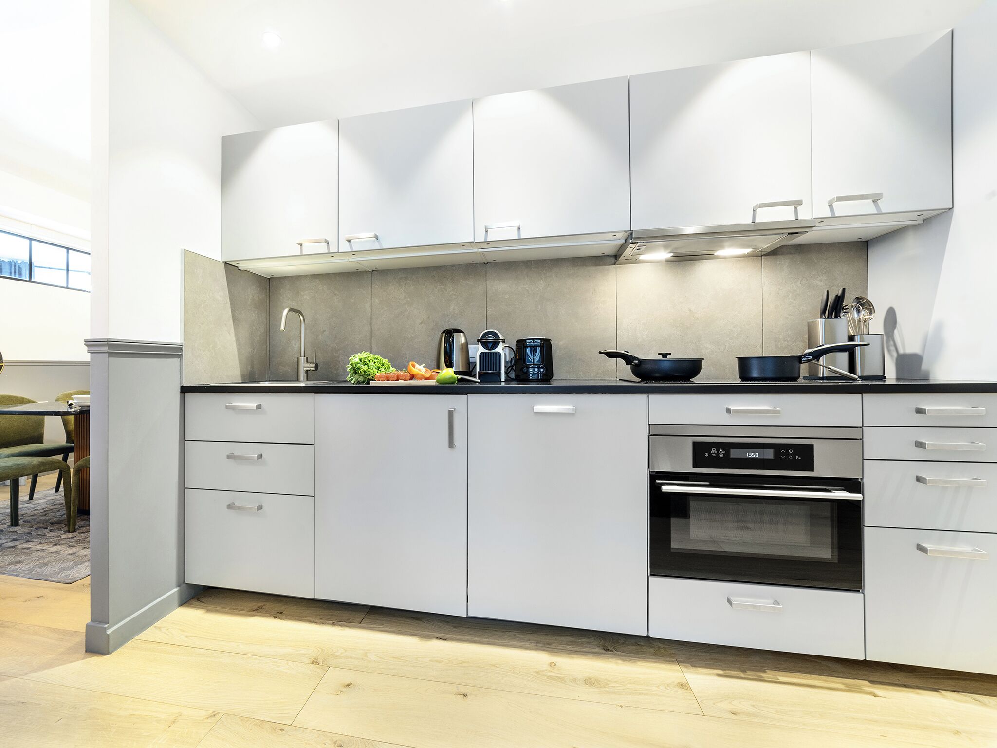 Una cucina moderna con mobili bianchi, forno integrato e macchina da caffè.