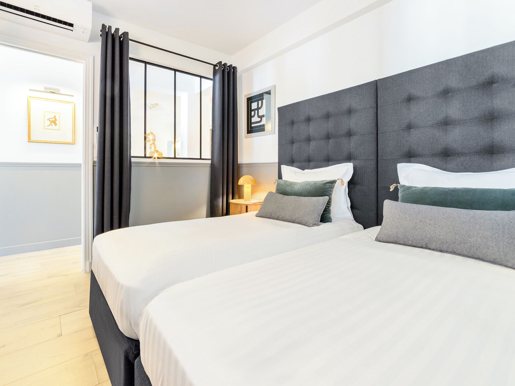 Ein Hotelzimmer mit zwei Betten, einem Nachttisch, einer Lampe und einem Fenster mit Vorhängen.