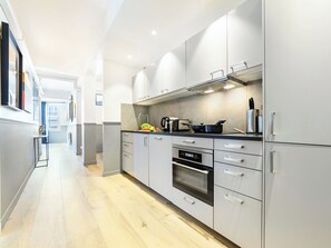 A modern kitchen with stainless steel appliances, a wooden floor, and a view of the hallway.