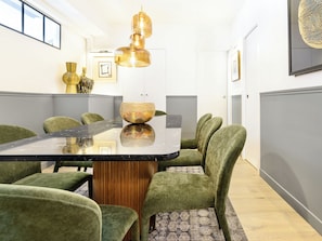 A conference room with a glass-top table, green upholstered chairs, and a hanging pendant light.