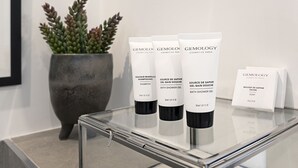 Une table en verre sur laquelle sont posées trois bouteilles de gel douche Gemology et une boîte de savon.