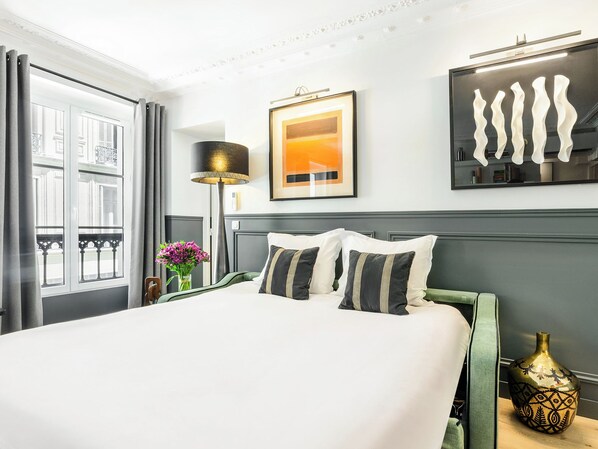 A hotel room with a large bed, a bedside lamp, a framed picture, and a vase with flowers.
