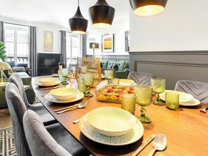 Uma sala de jantar com uma mesa comprida posta para refeição, com copos de padrão decorativo e um arranjo central ornamental.