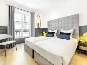 Habitación de hotel con una cama grande, dos mesitas de noche, una silla y un ventanal con cortinas.