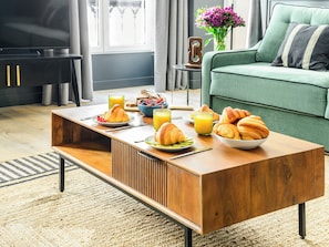 Una sala de estar moderna con una mesa de centro de madera, un sofá verde y una zona de comedor con alimentos para el desayuno.