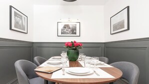 Un coin repas avec une table ronde dressée pour quatre personnes, des photos encadrées accrochées aux murs et un luminaire suspendu au-dessus.