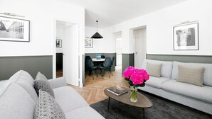 Un salon moderne avec un canapé gris, une table basse sur laquelle sont posés un livre et des fleurs, et un coin repas avec des chaises et une table.