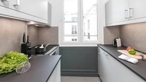 Une cuisine moderne avec des meubles gris, un plan de travail noir et une fenêtre donnant sur des immeubles.