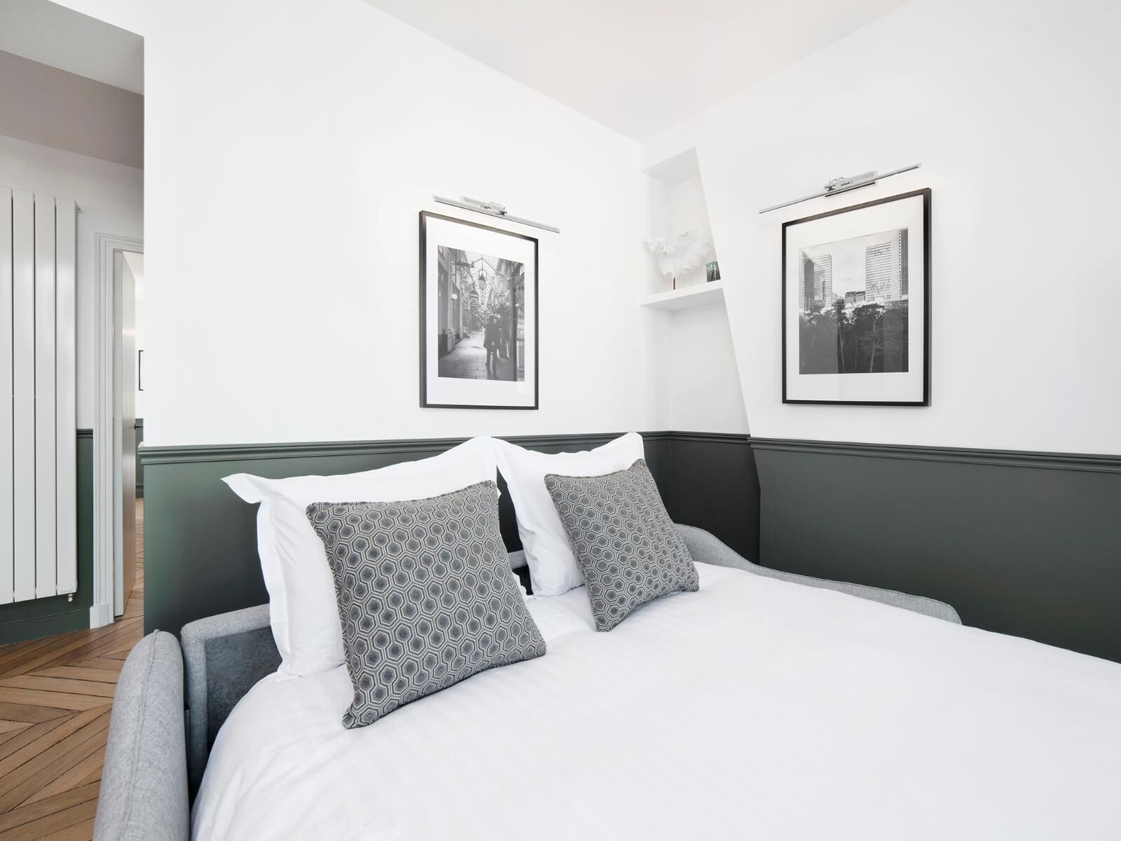 Een moderne hotelkamer met een groot bed, twee ingelijste foto’s aan de wand en een groene accentmuur.