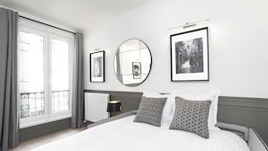 Een moderne hotelkamer met een groot bed, een ronde spiegel en twee ingekaderde foto's aan de muur.
