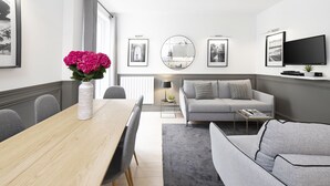 Een moderne woonkamer met een eethoek, een grijze bank en een flatscreen televisie die aan de muur is bevestigd.